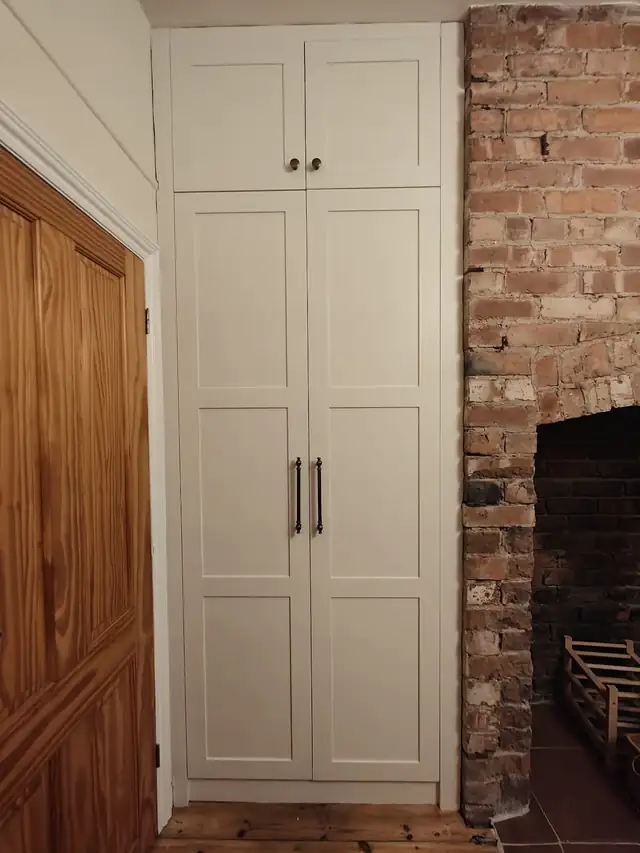 Tall painted shaker cupboard doors fitted in an alcove beside a brick chimney breast