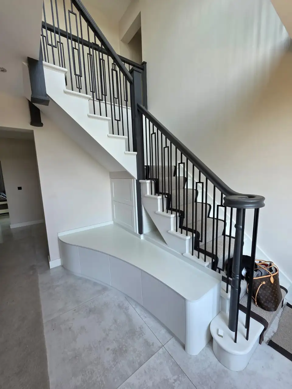 White staircase with black metal balustrade and a curved under stairs bench built by Grand Joinery Services