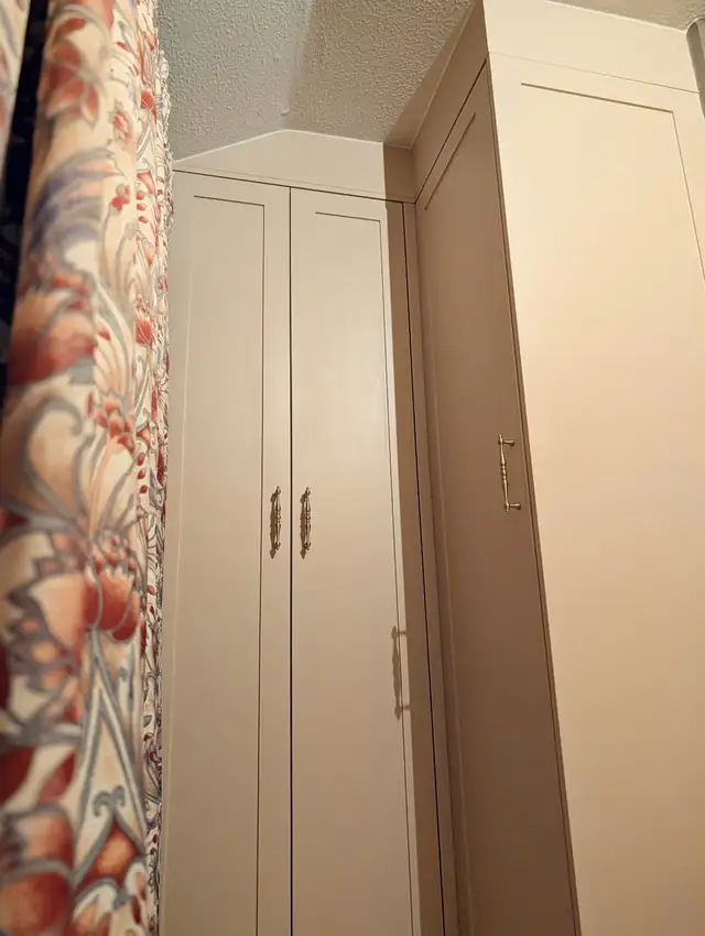 Cream fitted wardrobes with brass handles built into a bedroom alcove